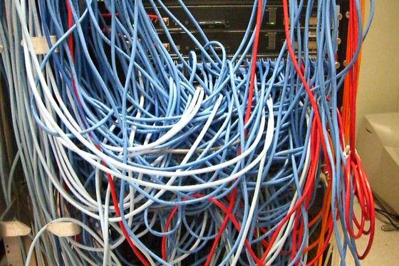 Serverschrank mit einem unübersichtlichen Gewirr aus blauen und roten Netzwerkkabeln