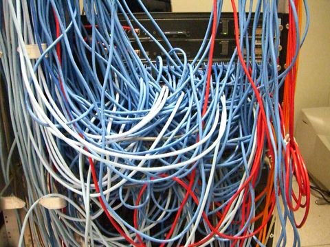 Serverschrank mit einem unübersichtlichen Gewirr aus blauen und roten Netzwerkkabeln