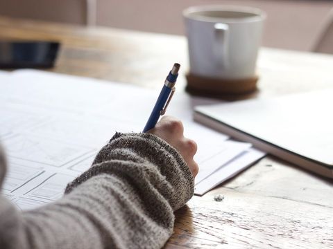 Hand mit Bleistift skizziert Seitenlayouts für eine Website, daneben Kaffeebecher und Notizbuch